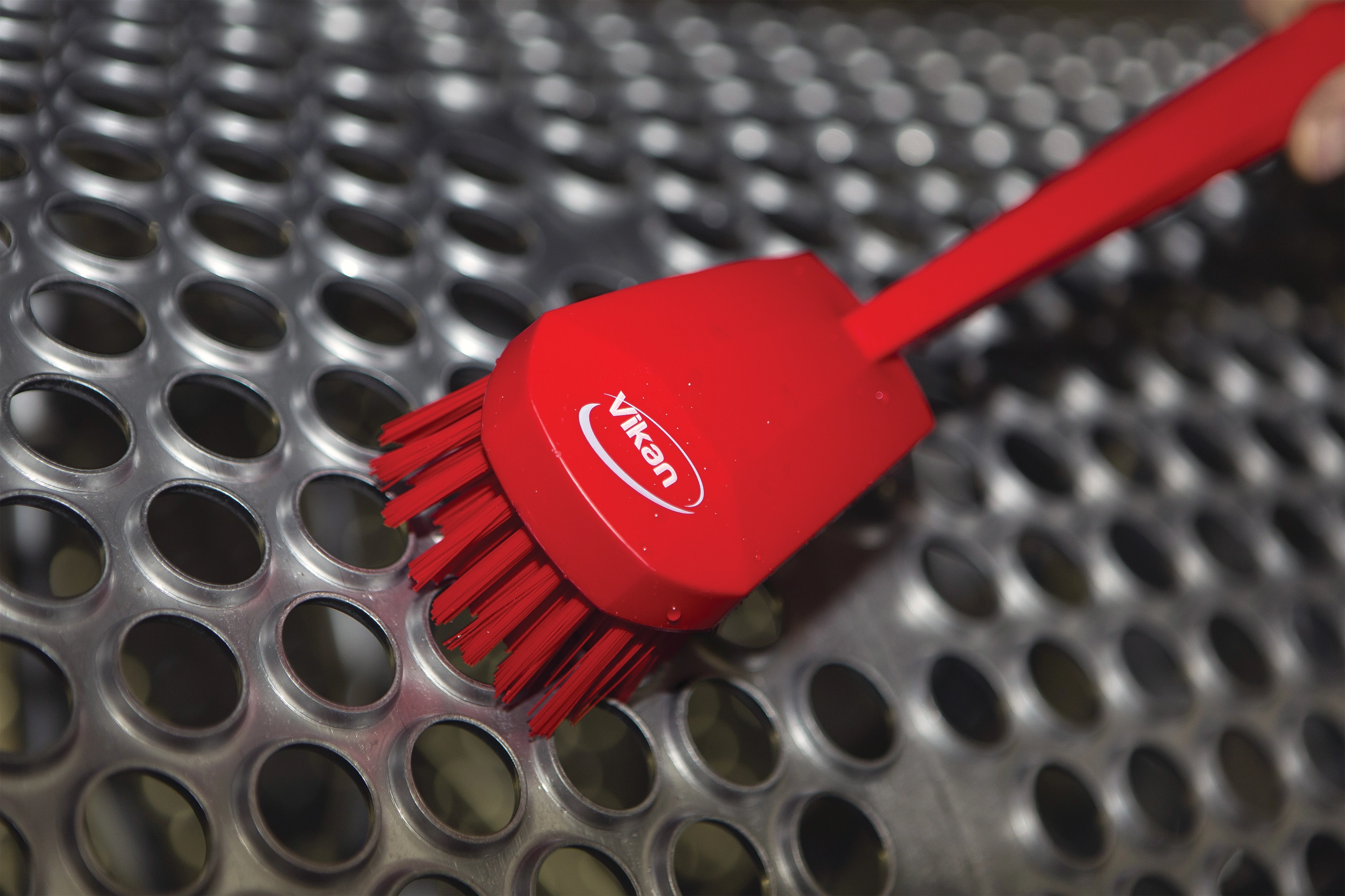 A red Vikan brush cleans a retort sheet in a food processing plant.