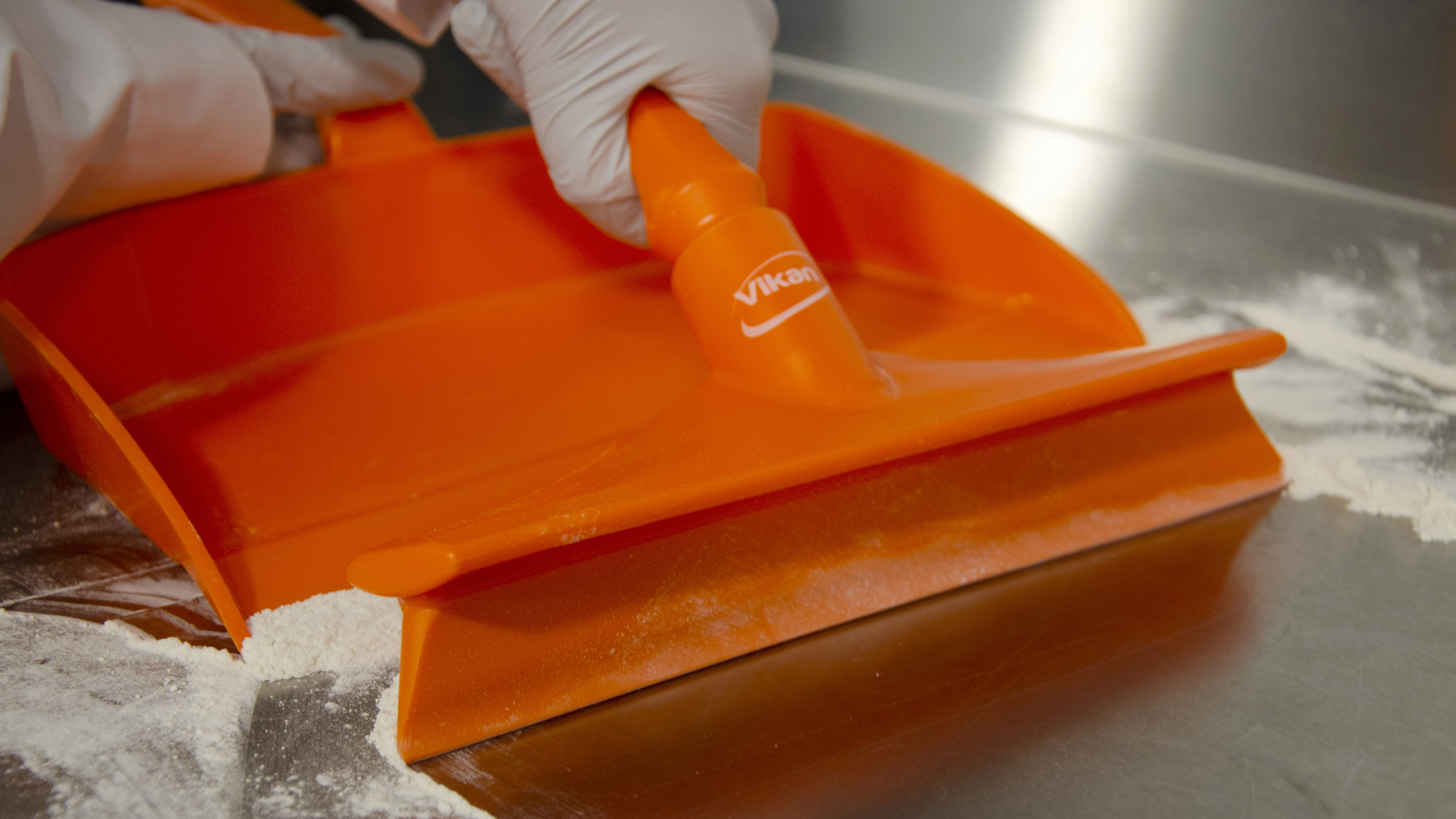 Vikan orange bench squeegee moving powder into an orange dustpan