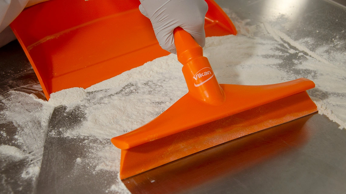 Orange Vikan bench squeegee removing powder from table